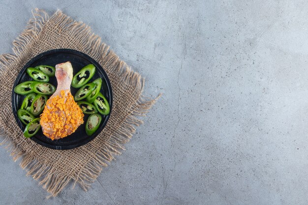 Marinated drumstick and sliced pepper on a plate on the burlap napkin , on the marble background. 