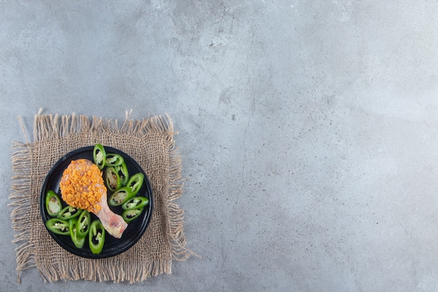 Marinated drumstick and sliced pepper on a plate on the burlap napkin , on the marble background. 