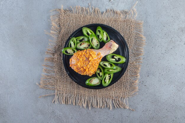 Marinated drumstick and sliced pepper on a plate on the burlap napkin , on the marble surface.