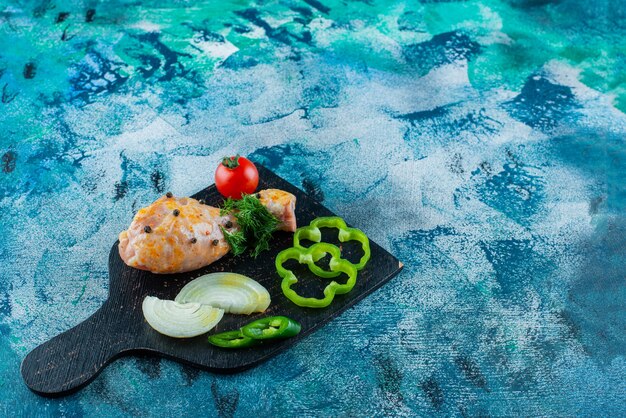 Marinated drumstick and sliced vegetables on a cutting board, on the blue background. 