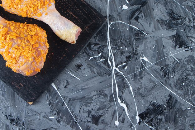 Marinated drumsticks on a cutting board next to spice bowls , on the marble background.