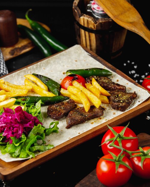 Marinated kebab served with french fries lettuce pickles grilled tomato and pepper