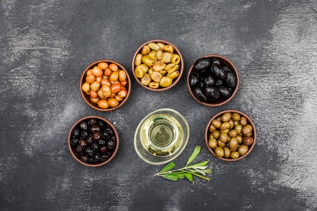 Marinated olives and olive oil in clay bowls and glass jar with olive tree branch top view on dark grey grunge