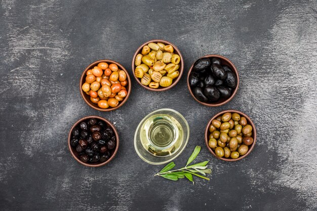 Marinated olives and olive oil in clay bowls and glass jar with olive tree branch top view on dark grey grunge