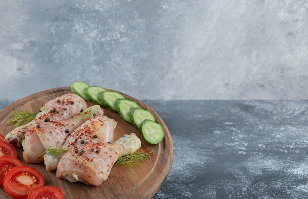 Marinated raw chicken drumstick with vegetable on wooden board.