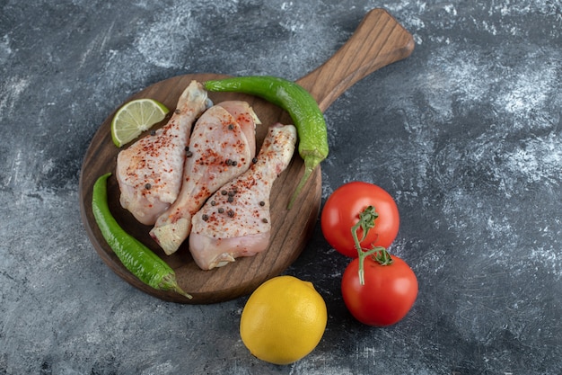 Free photo marinated raw chicken drumsticks with vegetable on grey background.