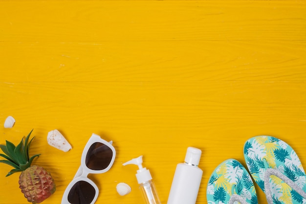 Marine travel , sunblock creams, slippers and pineapples placed on a yellow wooden floor.