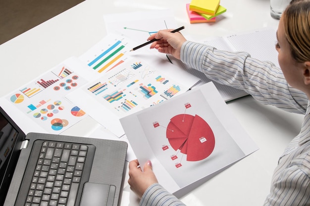 Маркетинговая бизнес-леди в полосатой рубашке в офисе с компьютером, указывающим на графики и диаграммы