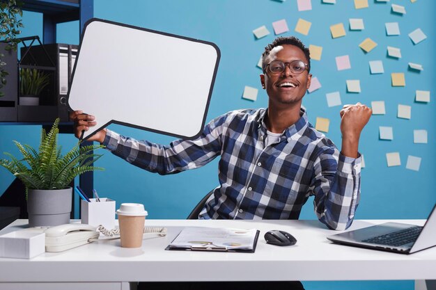 Marketing company happy smiling young adult person holding bubble sign while clenching fist triumphant.Management department team leader with cardboard speech bubble at work.