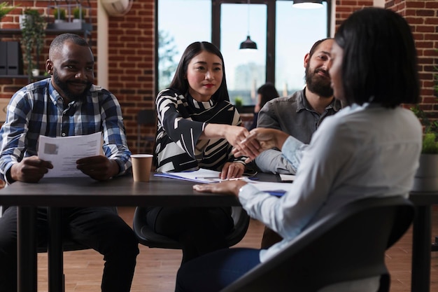 Marketing company recruiters sitting at desk in office while welcoming applicant to job interview. African american woman shaking recruitment team leader hand while making good first impression.