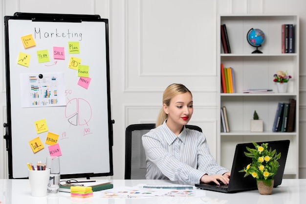 Free photo marketing smart cute business lady in striped shirt in office typing on computer and smiling