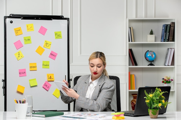 Marketing young cute blonde girl in grey suit in the office writing down notes