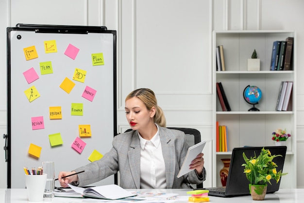 Free photo marketing young cute blonde girl in grey suit in the office writing something in notepad