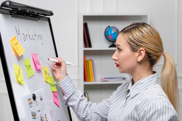 Бесплатное фото Маркетинговая молодая симпатичная бизнес-леди в полосатой рубашке в офисе пишет на борту