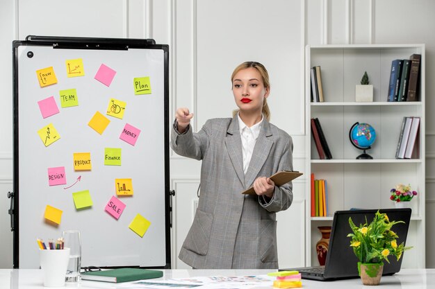 Marketing young pretty cute business lady in grey blazer in office pointing at a team member