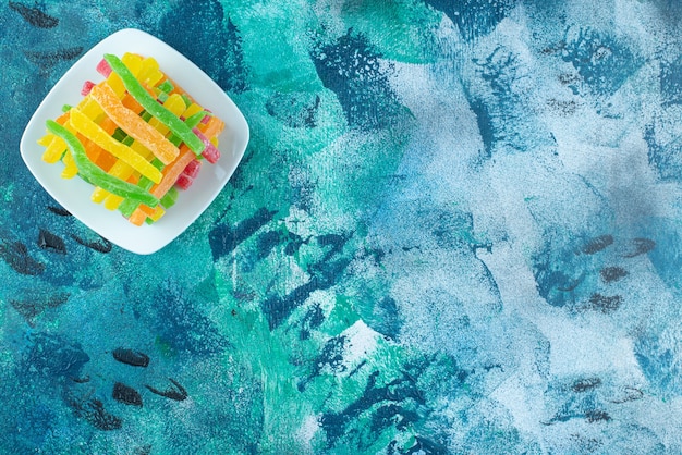 Marmalade in the form of colored sticks in a saucer, on the marble table.