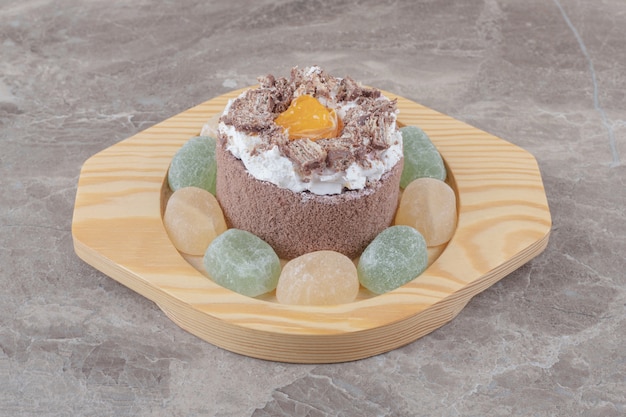 Marmelades around a small cake on a wooden platter on marble 