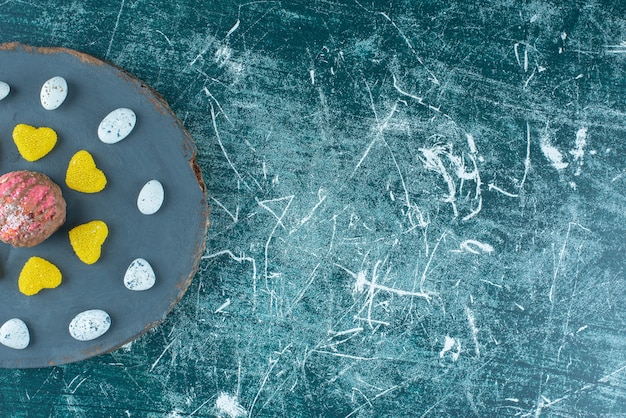 Marmelades and candy rocks around a chocolate coated cookie on a board on blue.