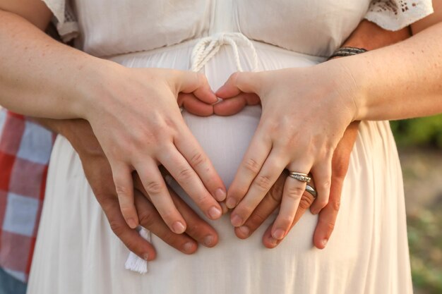여자의 임신 배꼽에 손으로 심장 모양을 형성하는 부부
