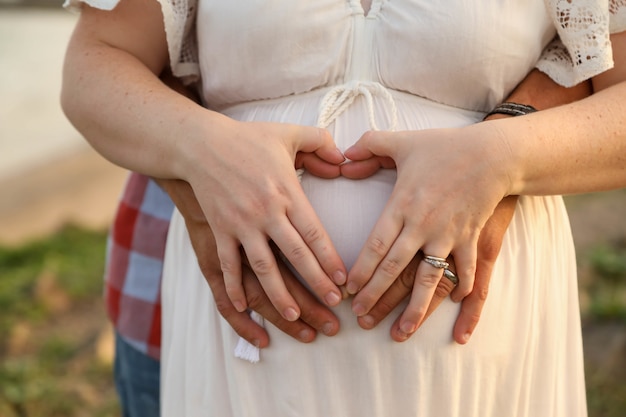 女性の妊娠中の腹に手でハートの形を形成する夫婦