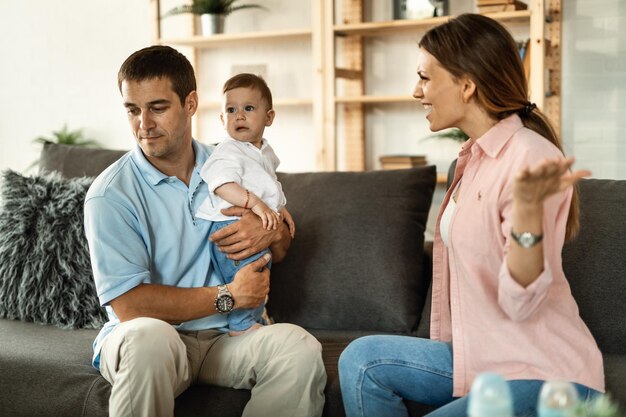 Married couple having an argument at home Man is holding their small son while woman is feeling angry and screaming at him