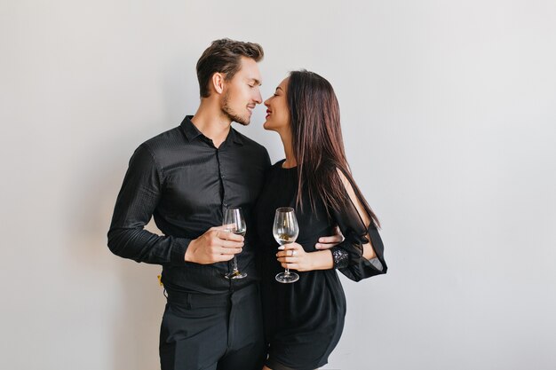 Married couple kissing at party, holding glasses of champagne in hands