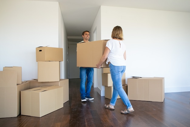 Married couple leaving apartment, carrying cartoon box to entrance together