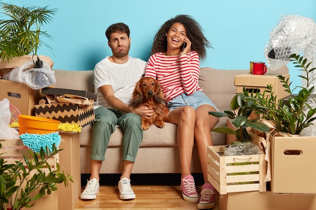 married couple on sofa with dog surrounded with cardboard boxes