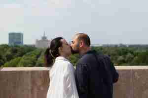 無料写真 美しい大都市の景色を楽しみながら観測点に立って結婚記念日を祝うタワーの屋上でキスする夫婦幸せなカップル。都市の建物のある風景