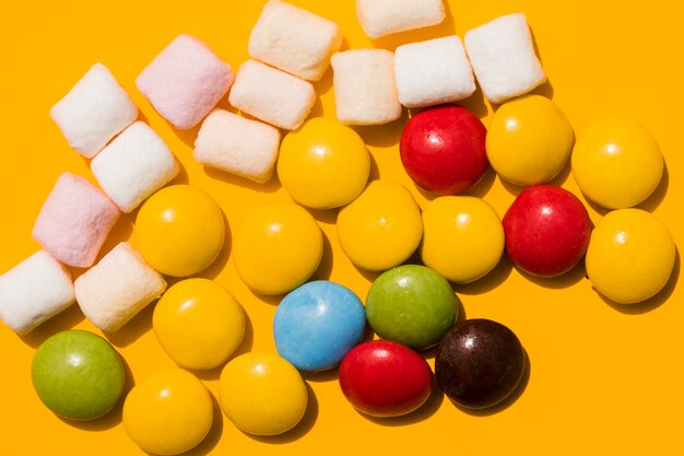 Marshmallow and colorful candies on yellow background
