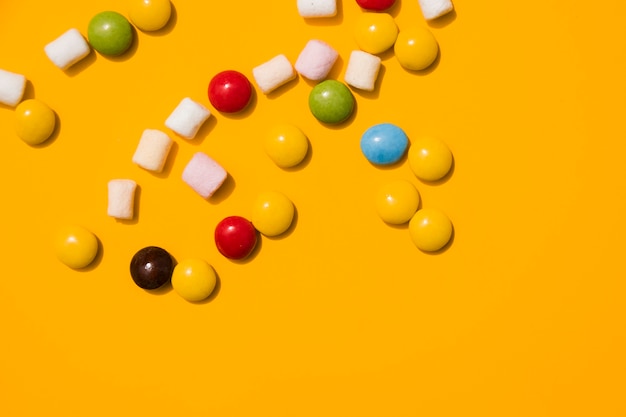 Marshmallow and colorful candies on yellow background