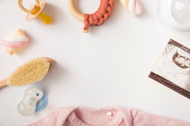 Marshmallow; pink baby onesie; brush; pacifier; milk bottle and toy on white background