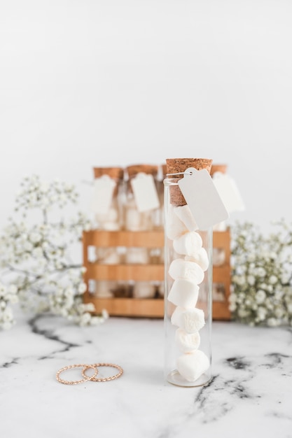 Marshmallow in the test tube with blank tag and wedding rings against white background