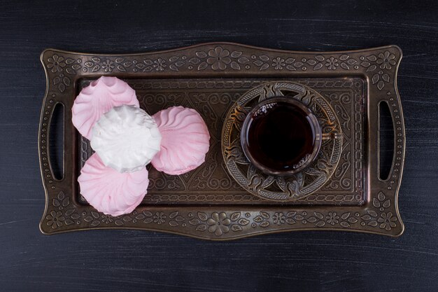 Marshmallows with a glass of tea in a metallic platter on a black surface