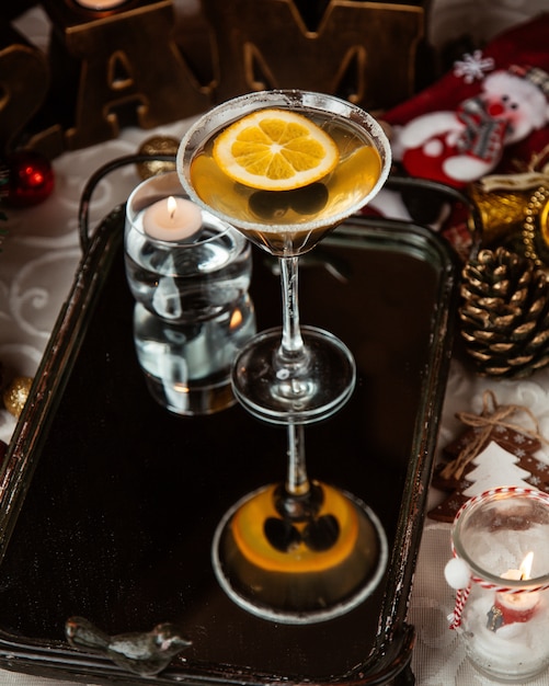 A martini glass of alcohol drink with black olive and lemon slice