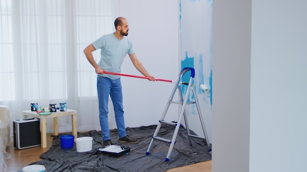 Masaking blue paint with roller brush dipped in white paint. Handyman renovating. Apartment redecoration and home construction while renovating and improving. Repair and decorating.