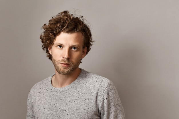 Masculine beauty, style and fashion concept. Fashionable 25 year old hipster guy with stubble and blue eyes posing isolated against copyspace wall , wearing stylish knitted sweater