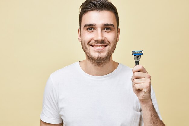 Masculinity, beauty and skin care concept. Portrait of handsome young male with bristle with broad smile holding shaving stick, going to shave beard in the morning before work