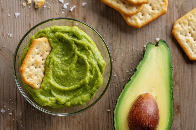 Mashed avocado guacamole sauce in bowl with crackers.