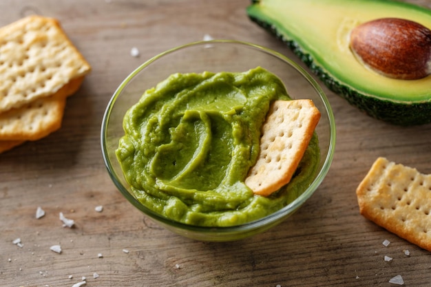 Mashed avocado guacamole sauce in bowl with crackers