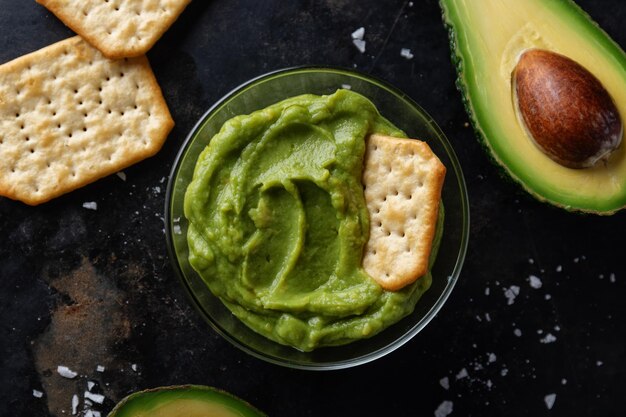 Mashed avocado guacamole sauce in bowl with crackers