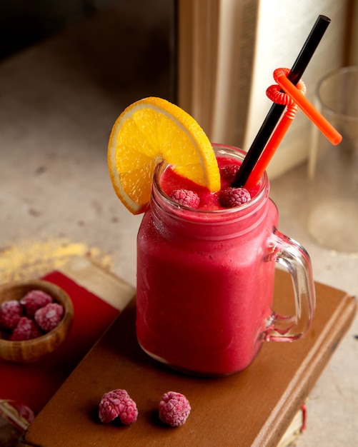 A mason jar with raspberry smoothie garnished with raspberry and orange slice