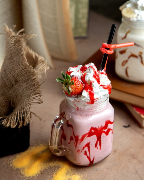 A mason jar with strawberry milkshake with strawberry syrup whipped cream and strawberry