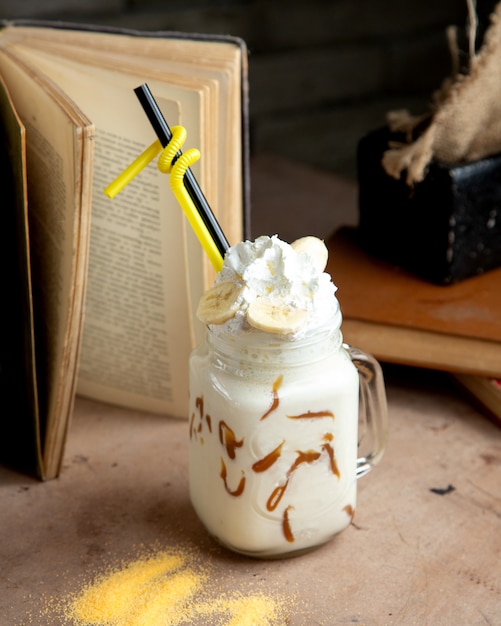 A mason jar with vanilla milkshake and chocolate syrup whipped cream and banana
