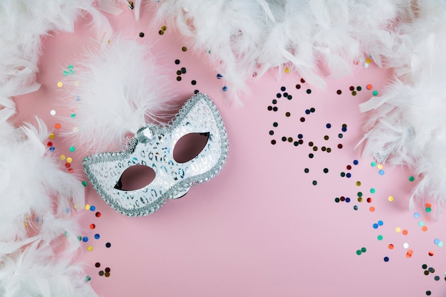 Free photo masquerade carnival feather mask with colorful confetti and boa feather on pink background