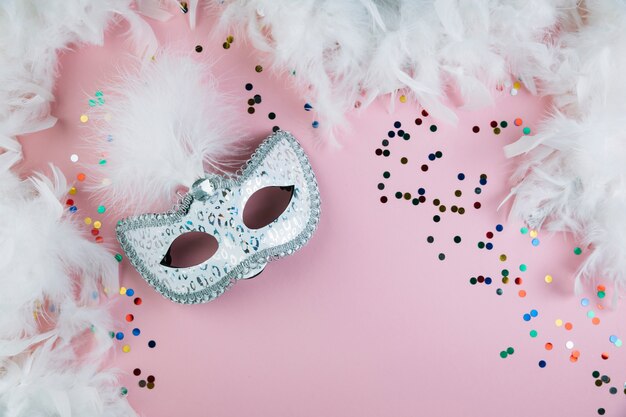 ピンクの背景にカラフルな紙吹雪とボアの羽を持つ仮面舞踏会カーニバル羽マスク