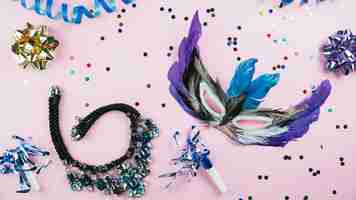 Бесплатное фото Маскарадная маска из карнавальных перьев с конфетти и колье на розовом фоне