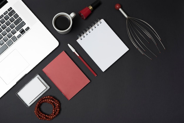 Massage tool; laptop; stationery; coffee cup; bracelet and nail varnish over black desk