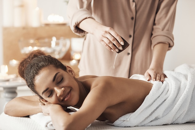 Foto gratuita massaggiatore che versa olio facendo massaggio per la bella donna africana nel salone spa.