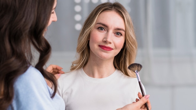 Master applying makeup to smiling blond woman